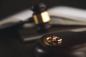 A gavel and two wedding rings on a wooden surface, symbolising the start of family court divorce proceedings and the legal stages that follow